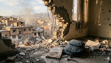View of damaged houses in Qeshlaq-Pol through a shattered school wall in Saqqez, with a dusty Farsi textbook in the foreground.